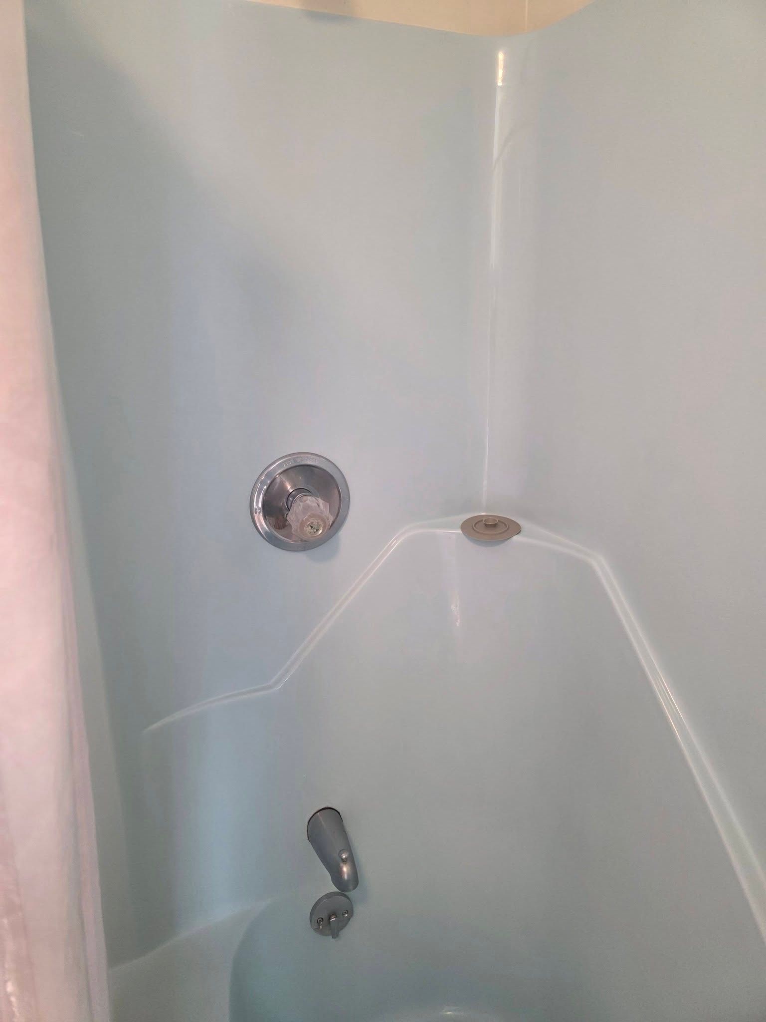 Empty light blue shower stall with chrome fixtures and built-in shelves