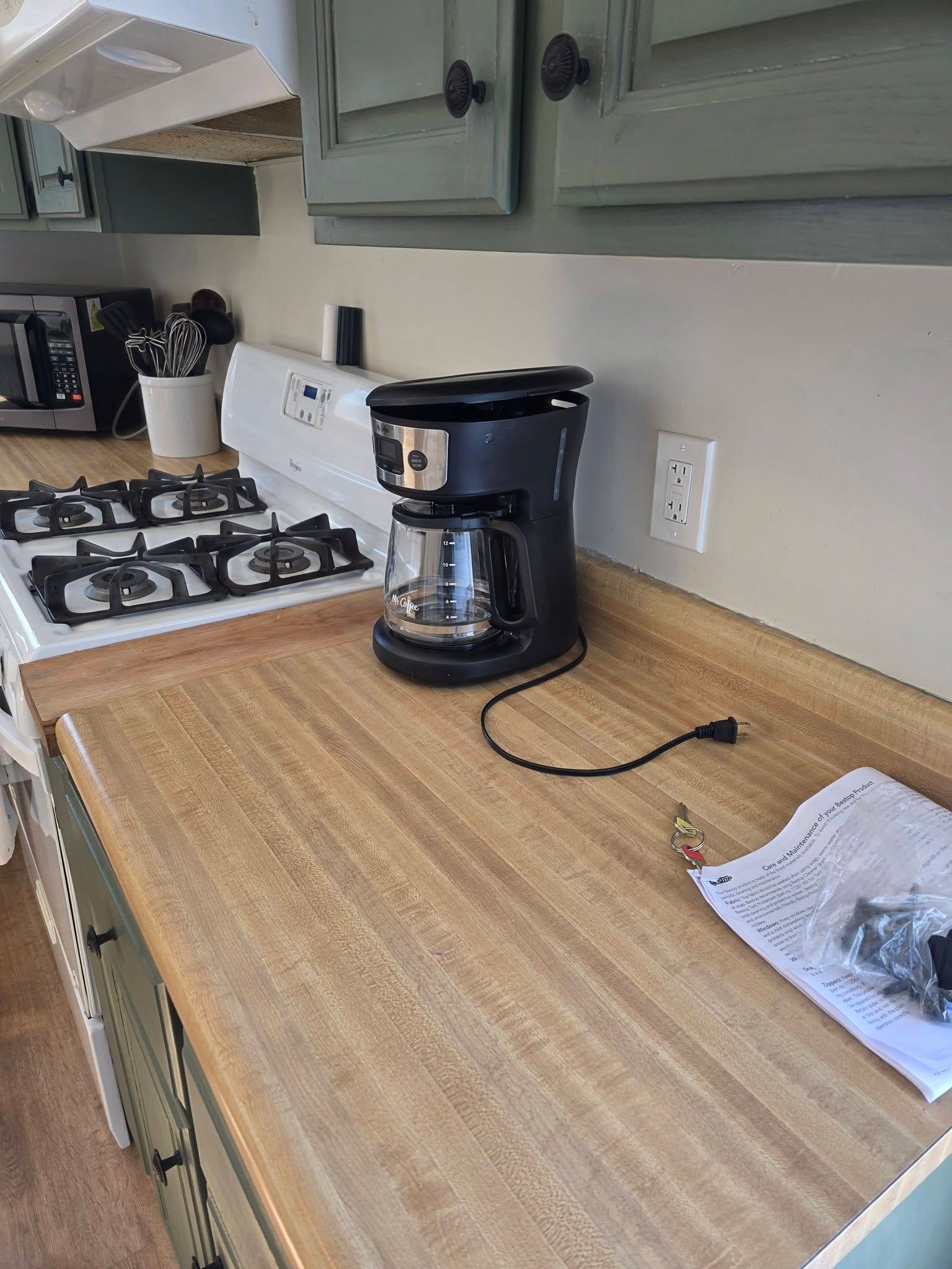 Kitchen counter with coffee maker, gas stove, and papers on a tan countertop.