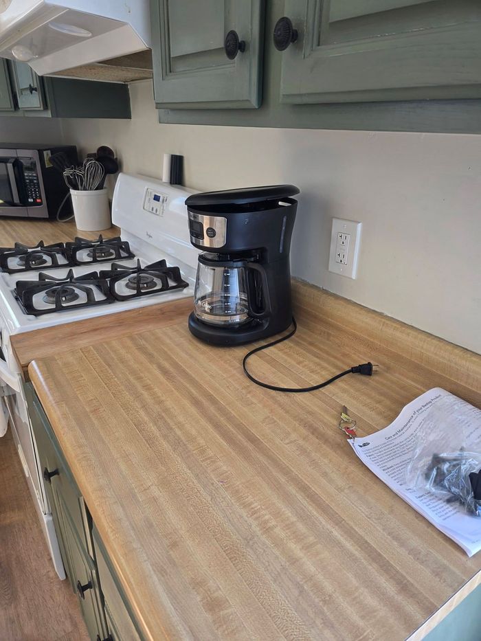 Kitchen counter with a coffee maker, gas stove, and papers on a wooden countertop.