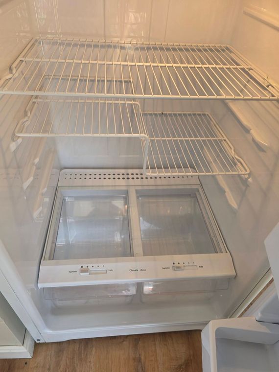 Empty white refrigerator interior with glass shelves and crisper drawers, door open.