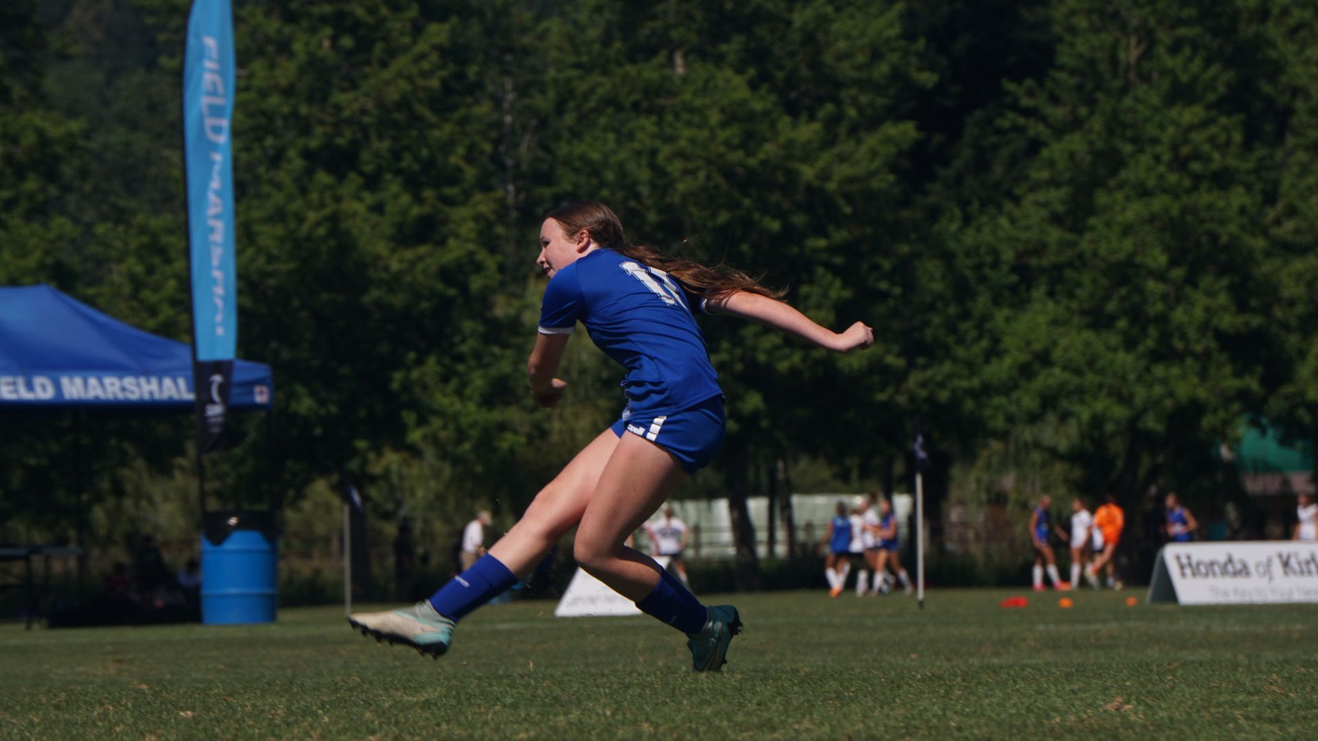 A girl is kicking a soccer ball on a field.