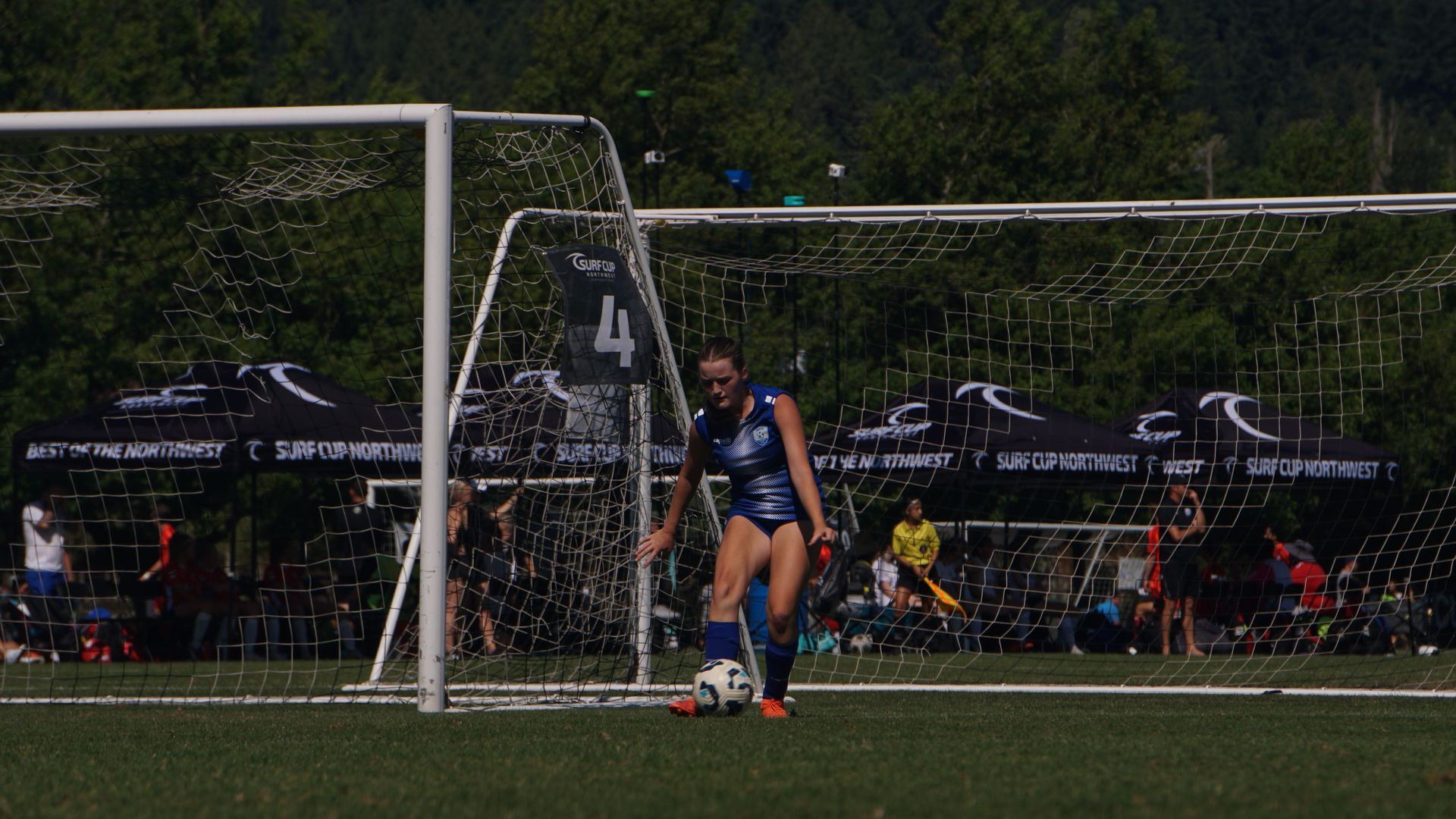 A woman is kicking a soccer ball in front of a goal.
