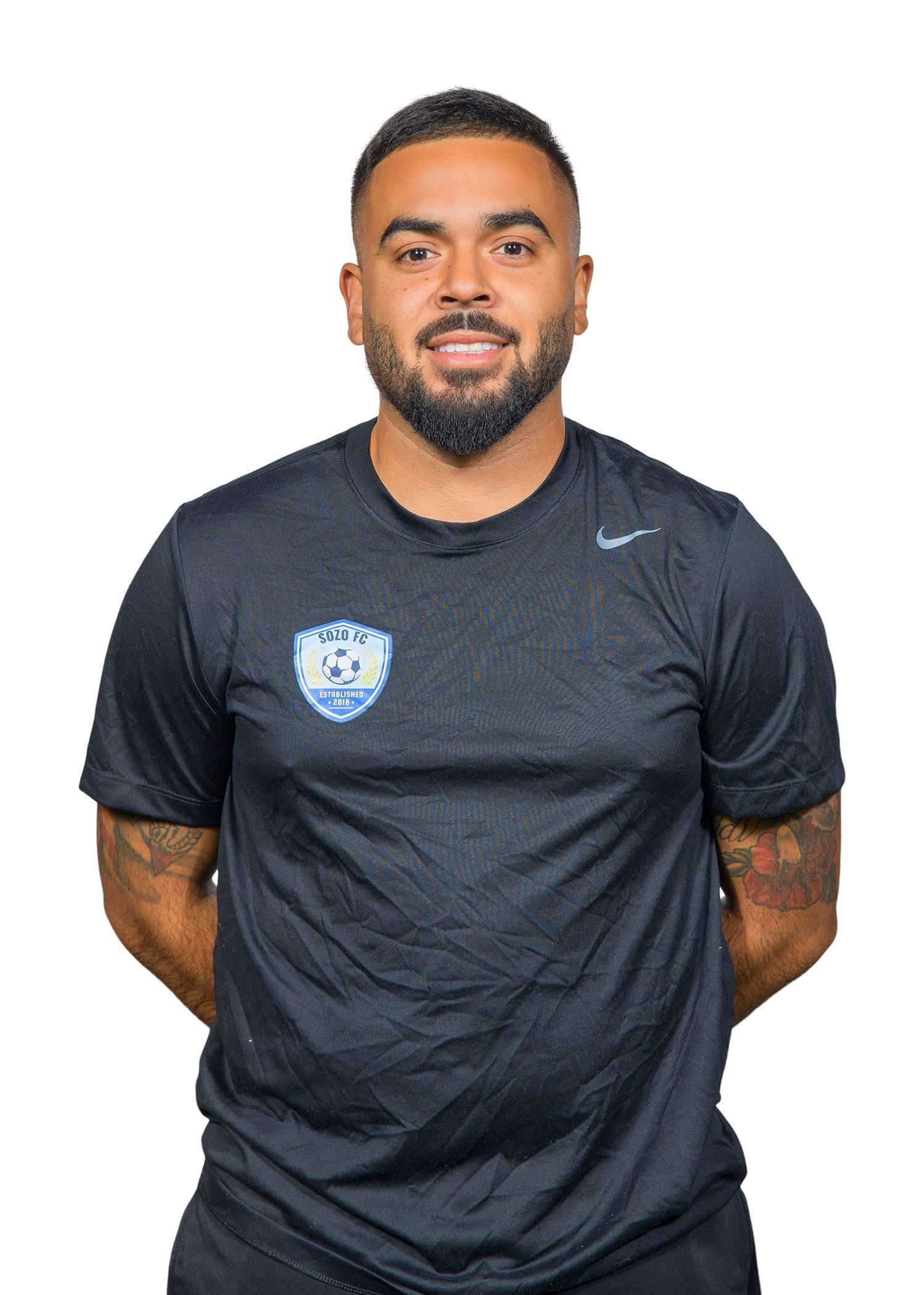 Man in black shirt with logo on chest, arms crossed, smiling.