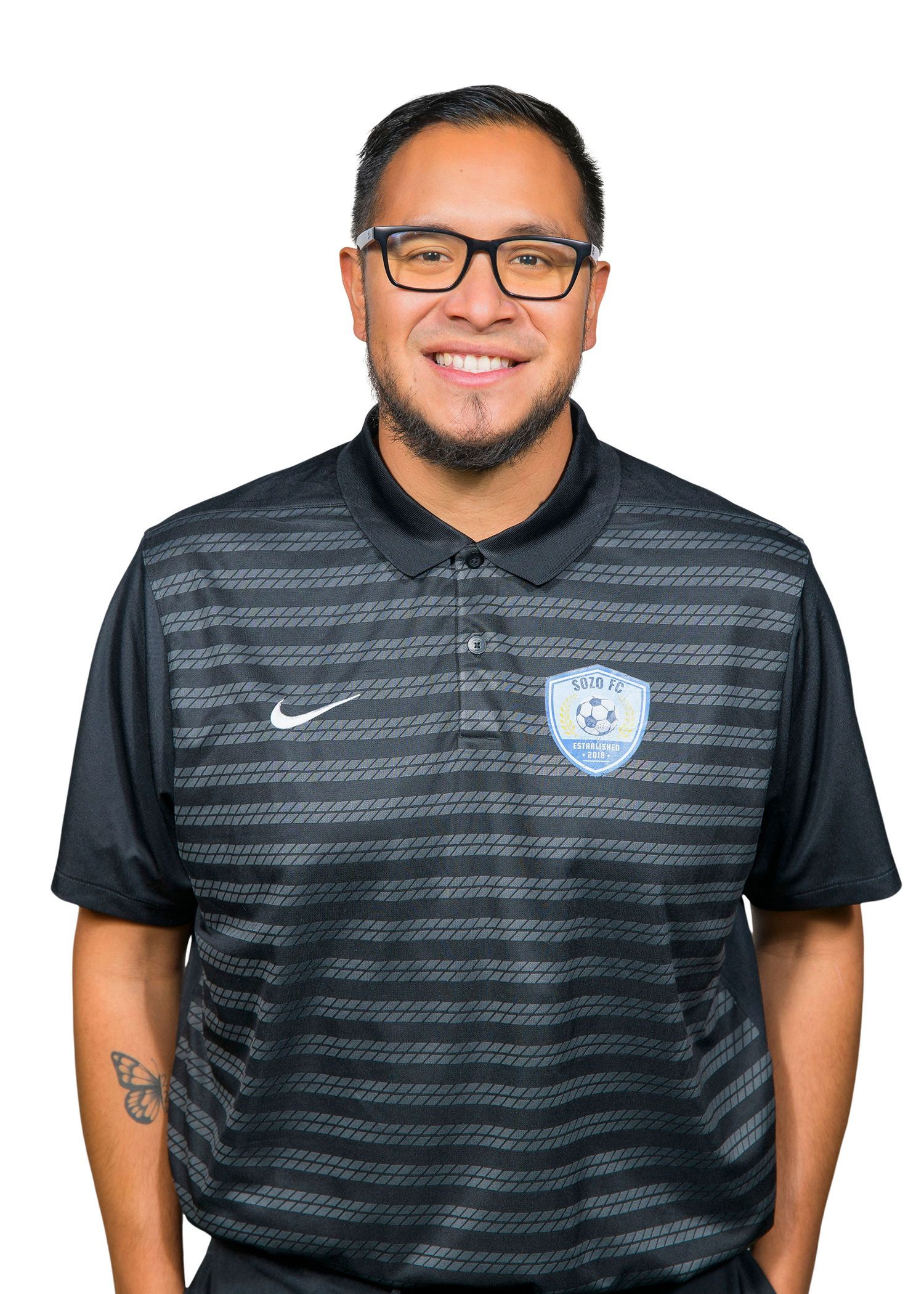 Person in a black striped polo shirt and glasses, smiling and standing against a plain white background.