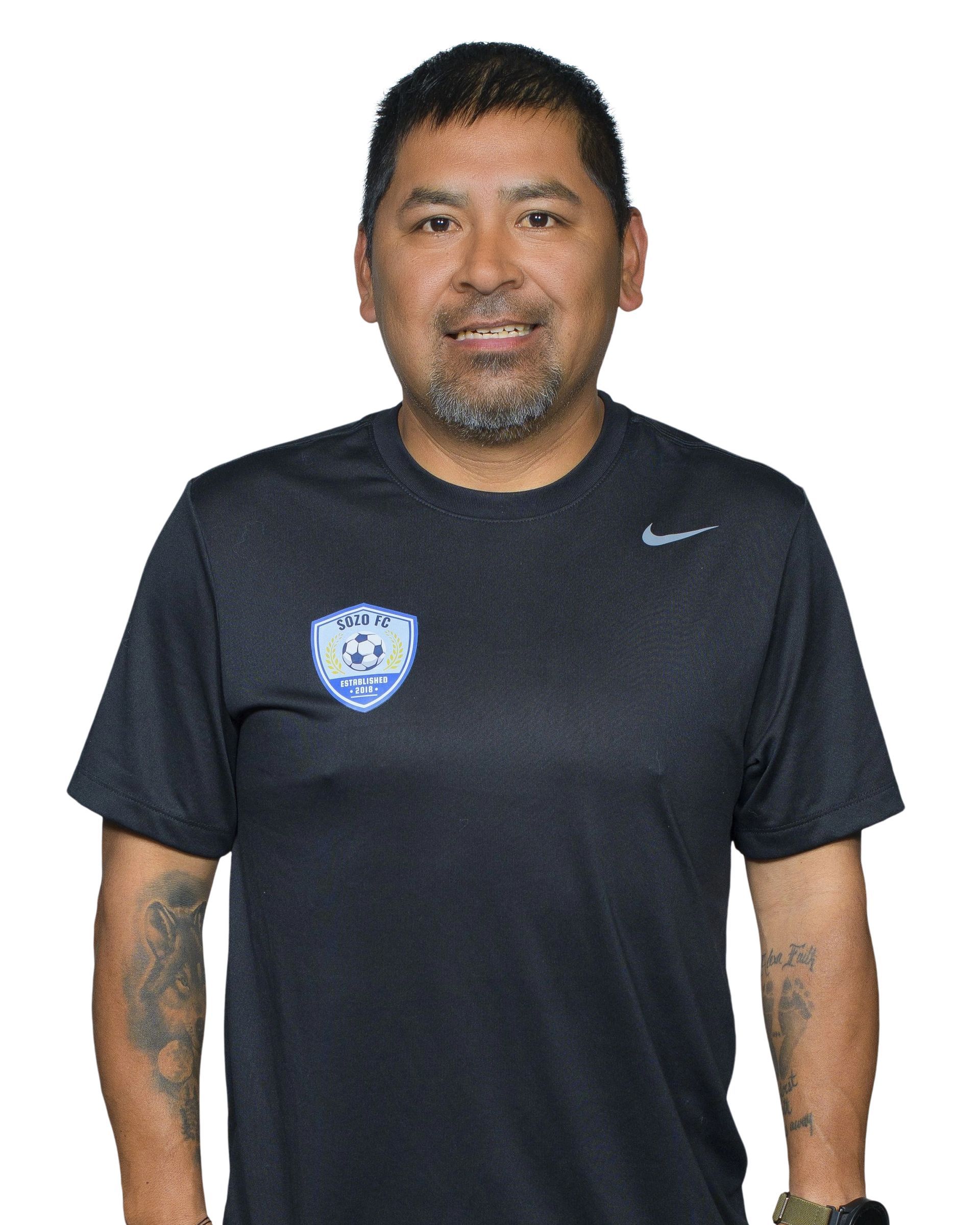 Man standing against a white background wearing a black athletic shirt with logos