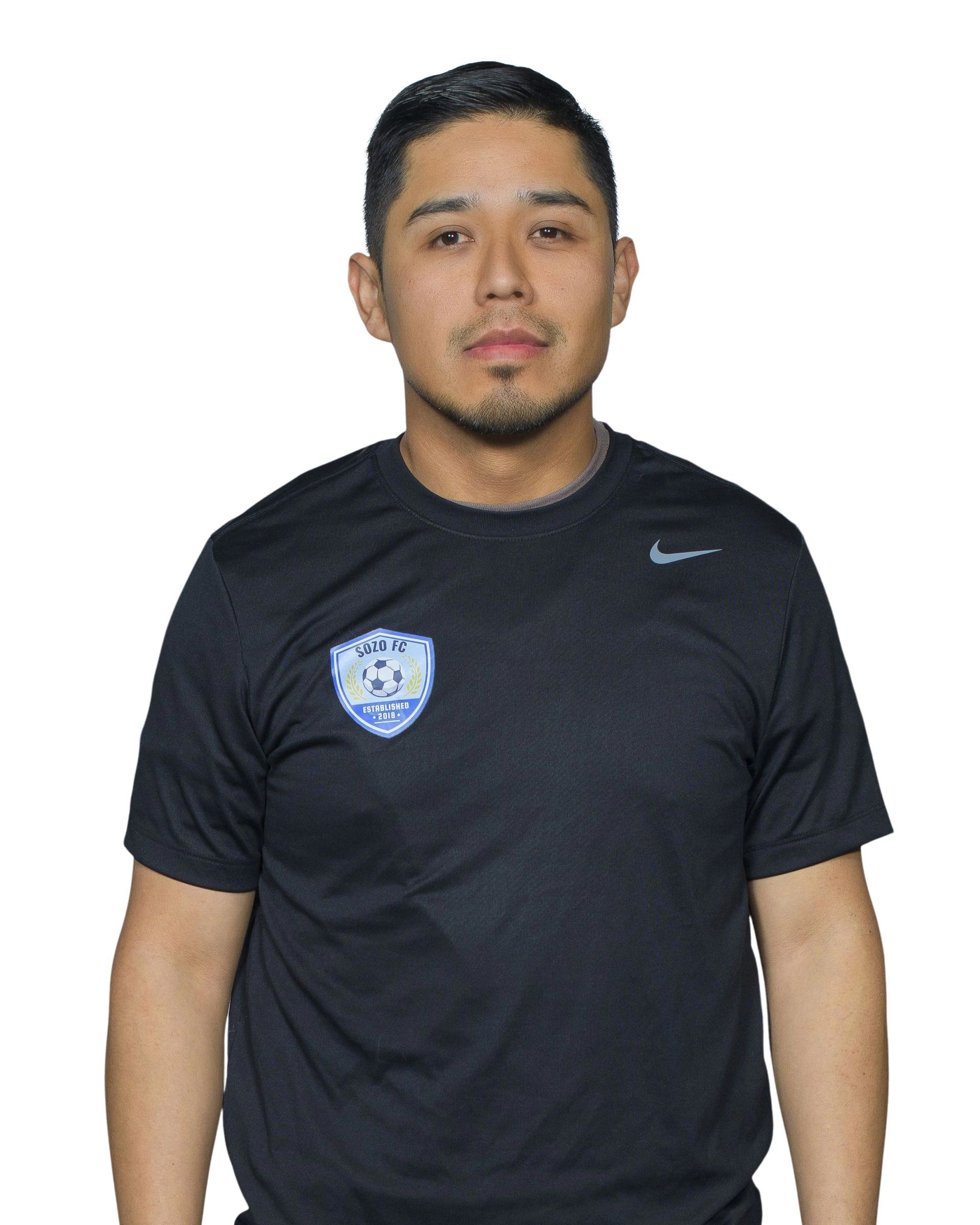 Man standing against a white background wearing a black Nike shirt with a blue crest badge