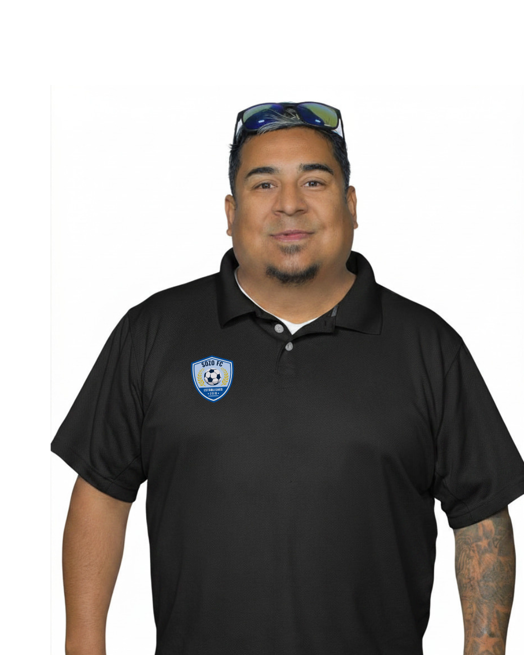 Man standing against a white background, wearing a black polo shirt with a blue logo and sunglasses on his head
