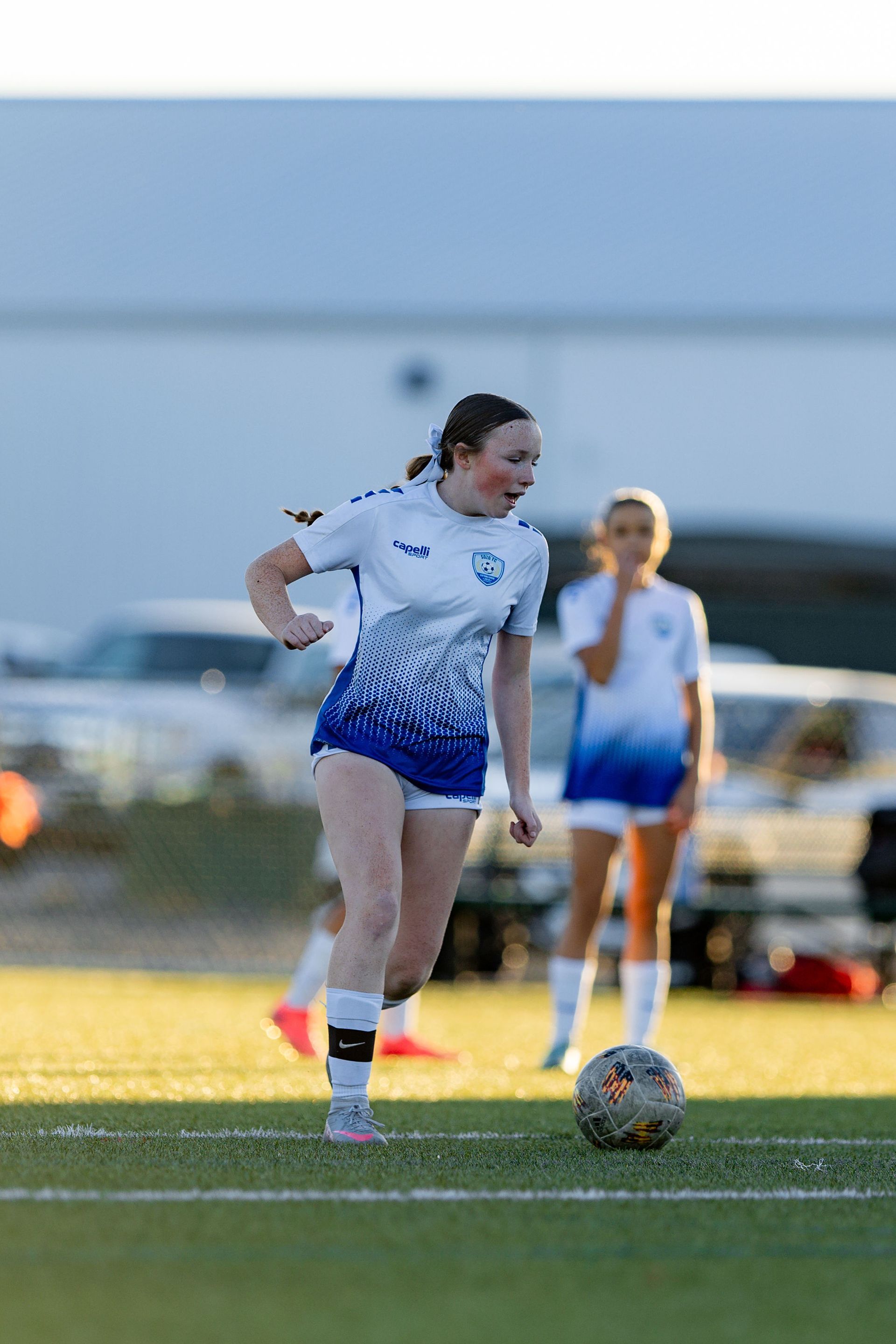 A woman is kicking a soccer ball on a field.