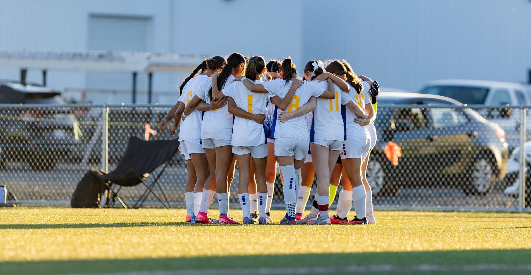 A group of female soccer players are huddled together on the field.
