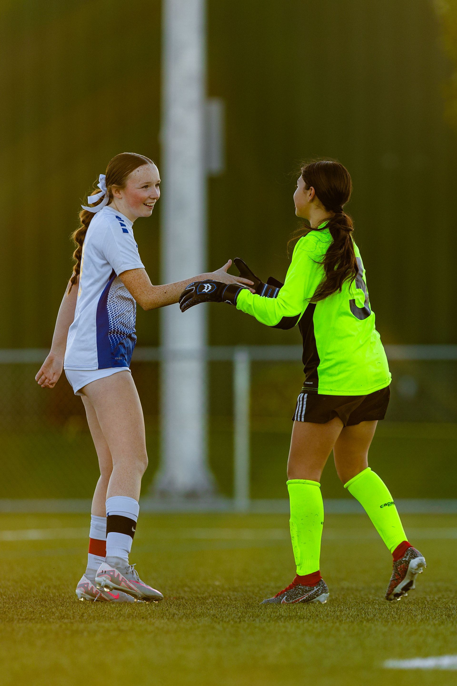 Two female soccer players are shaking hands on the field.