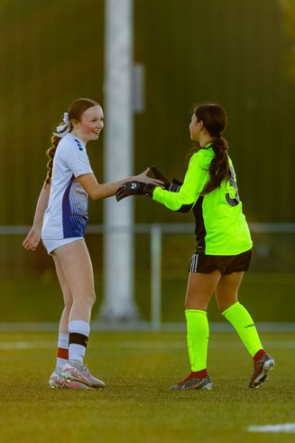 Two female soccer players are shaking hands on the field.
