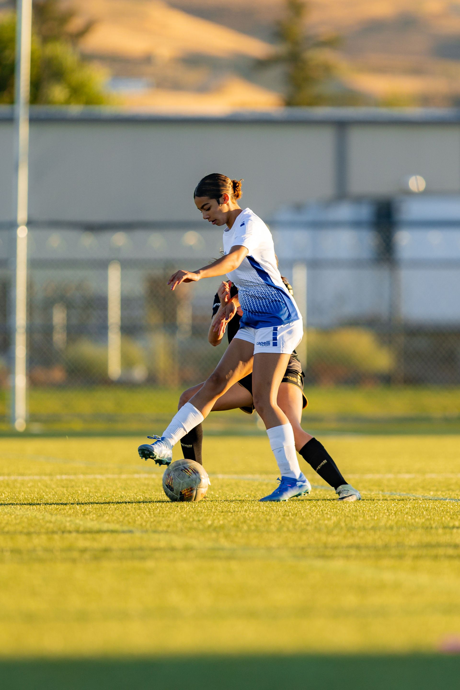 Two female soccer players are playing soccer on a field.