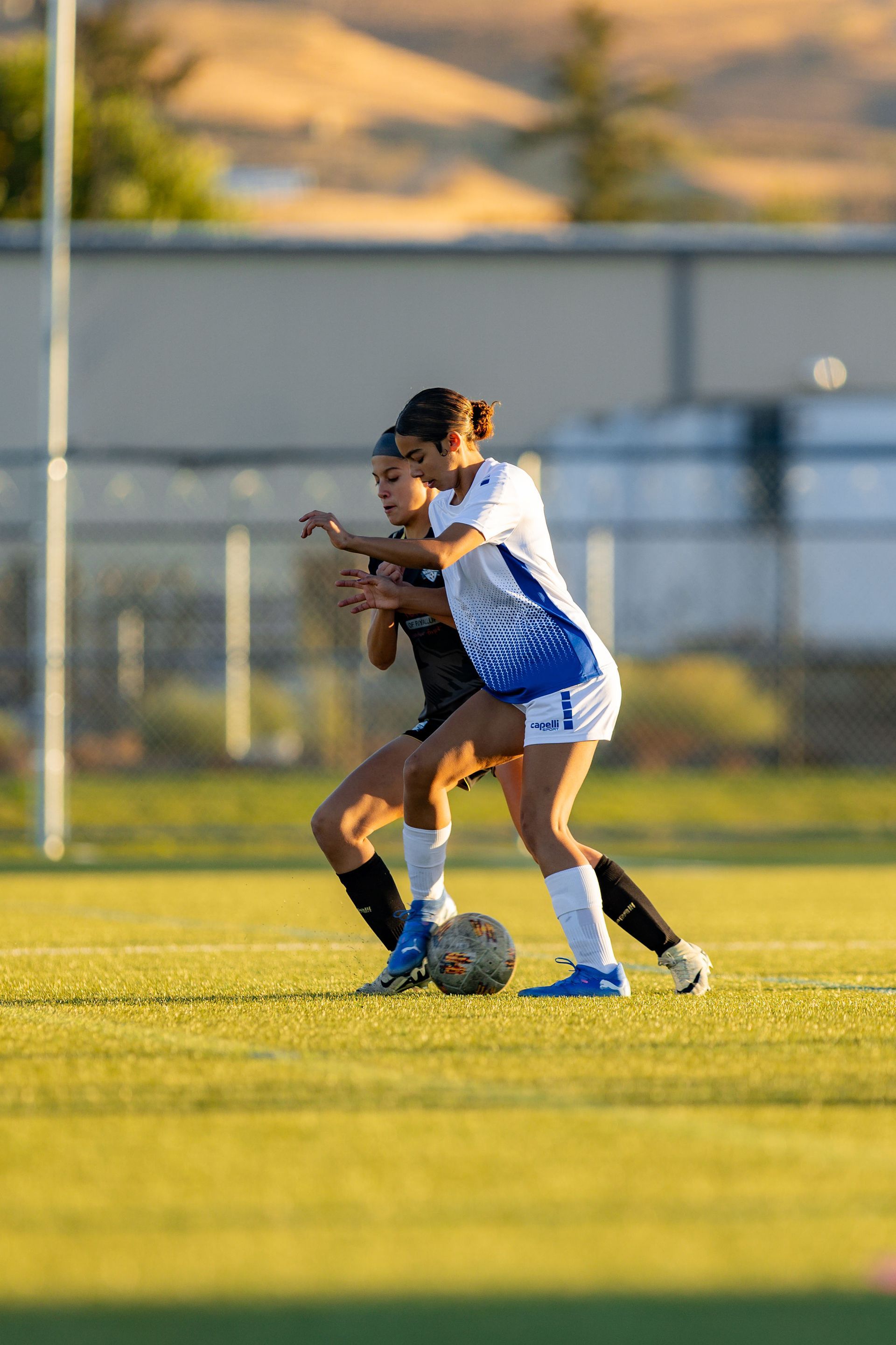 Two women are playing soccer on a field.