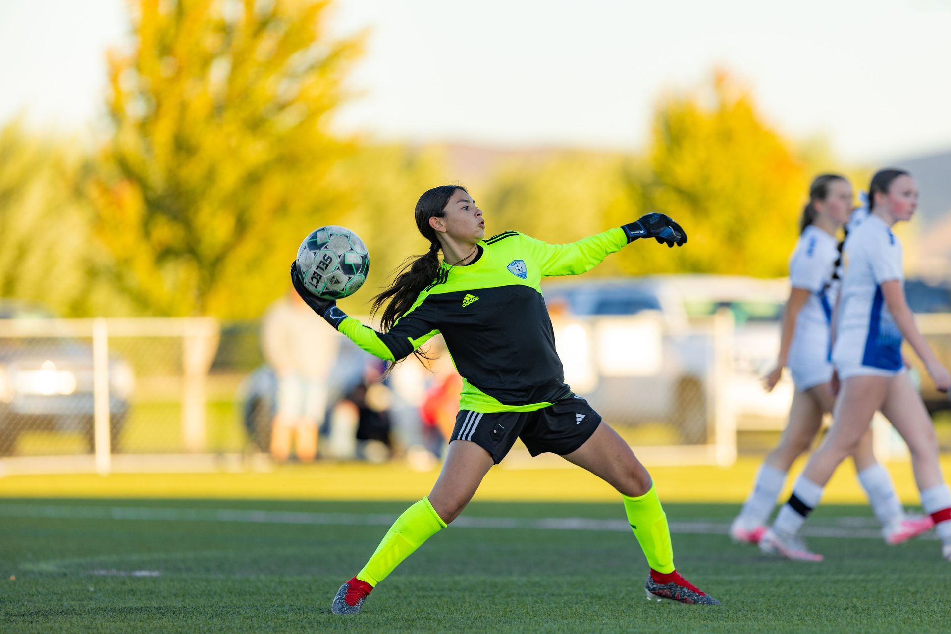 A female soccer goalie is catching a soccer ball on a field.
