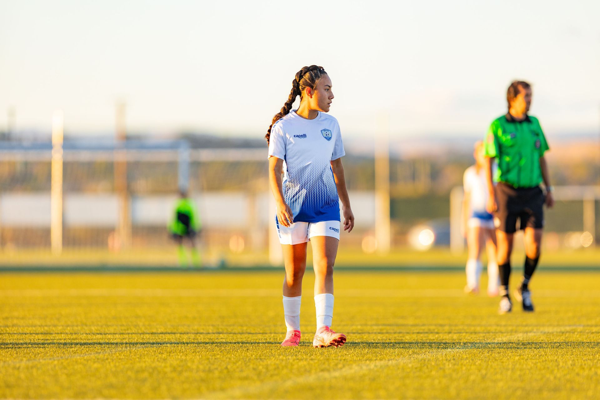 A girl is standing on a soccer field with a referee in the background.