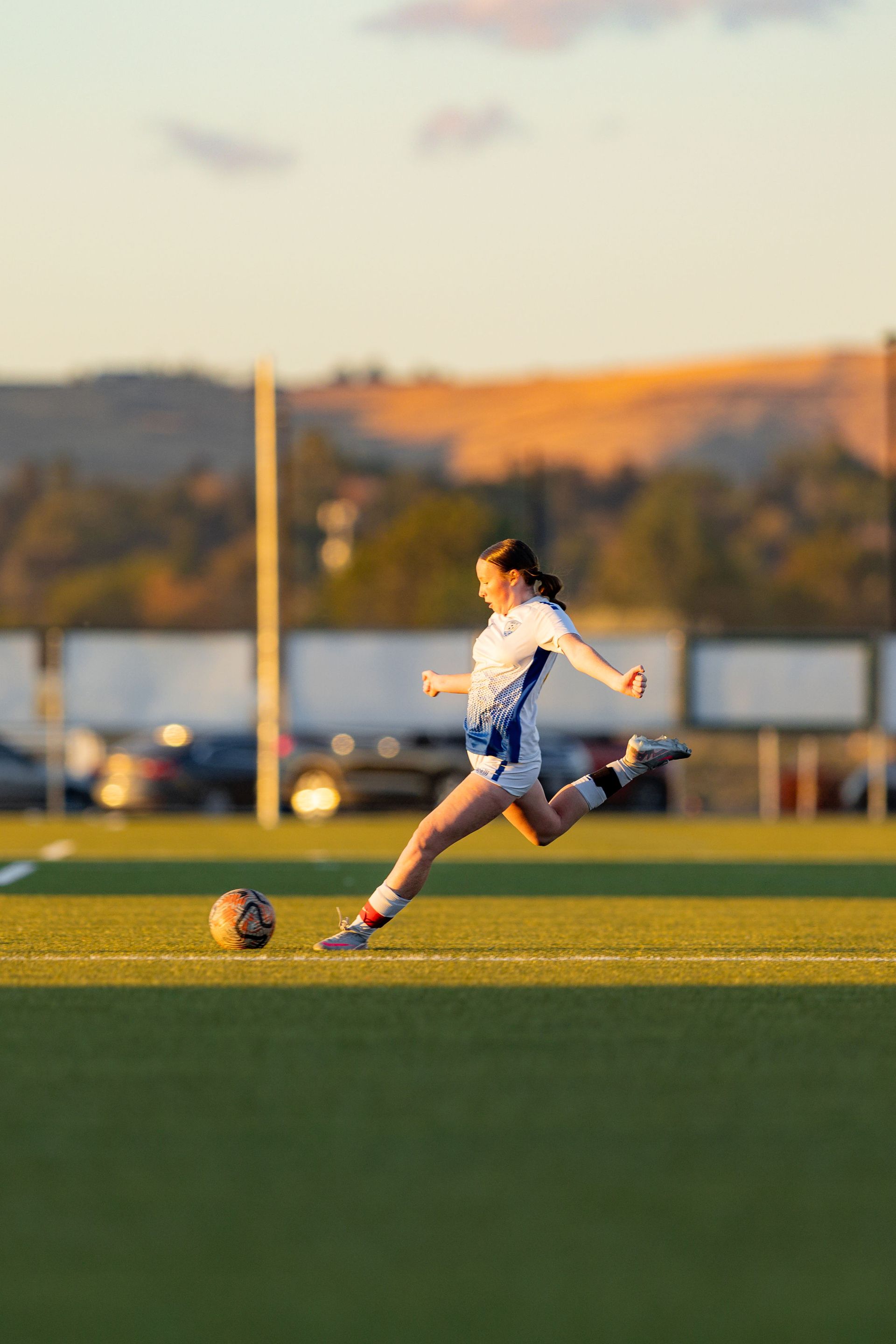 A woman is kicking a soccer ball on a field.