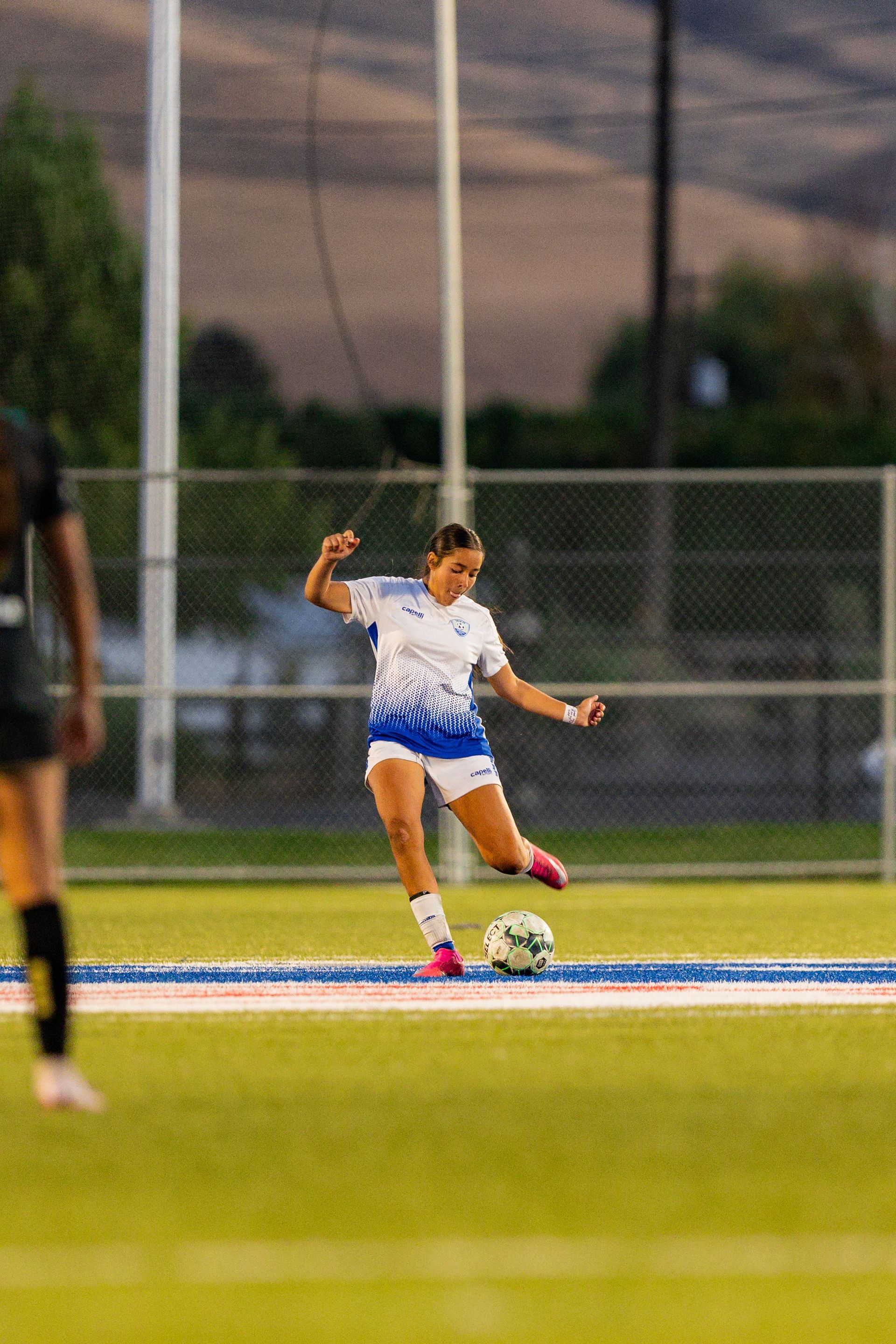 A woman is kicking a soccer ball on a field.