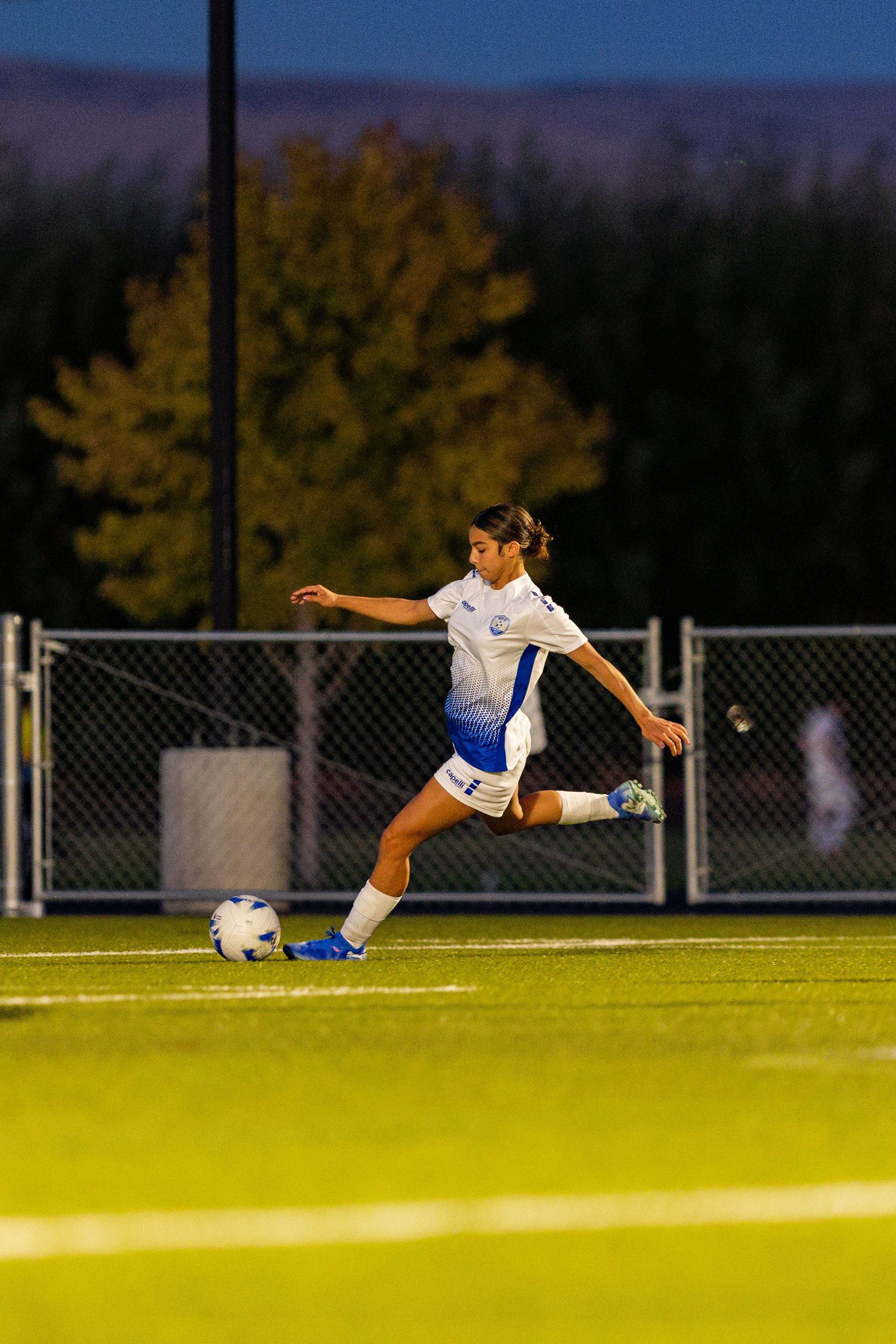 A woman is kicking a soccer ball on a field.