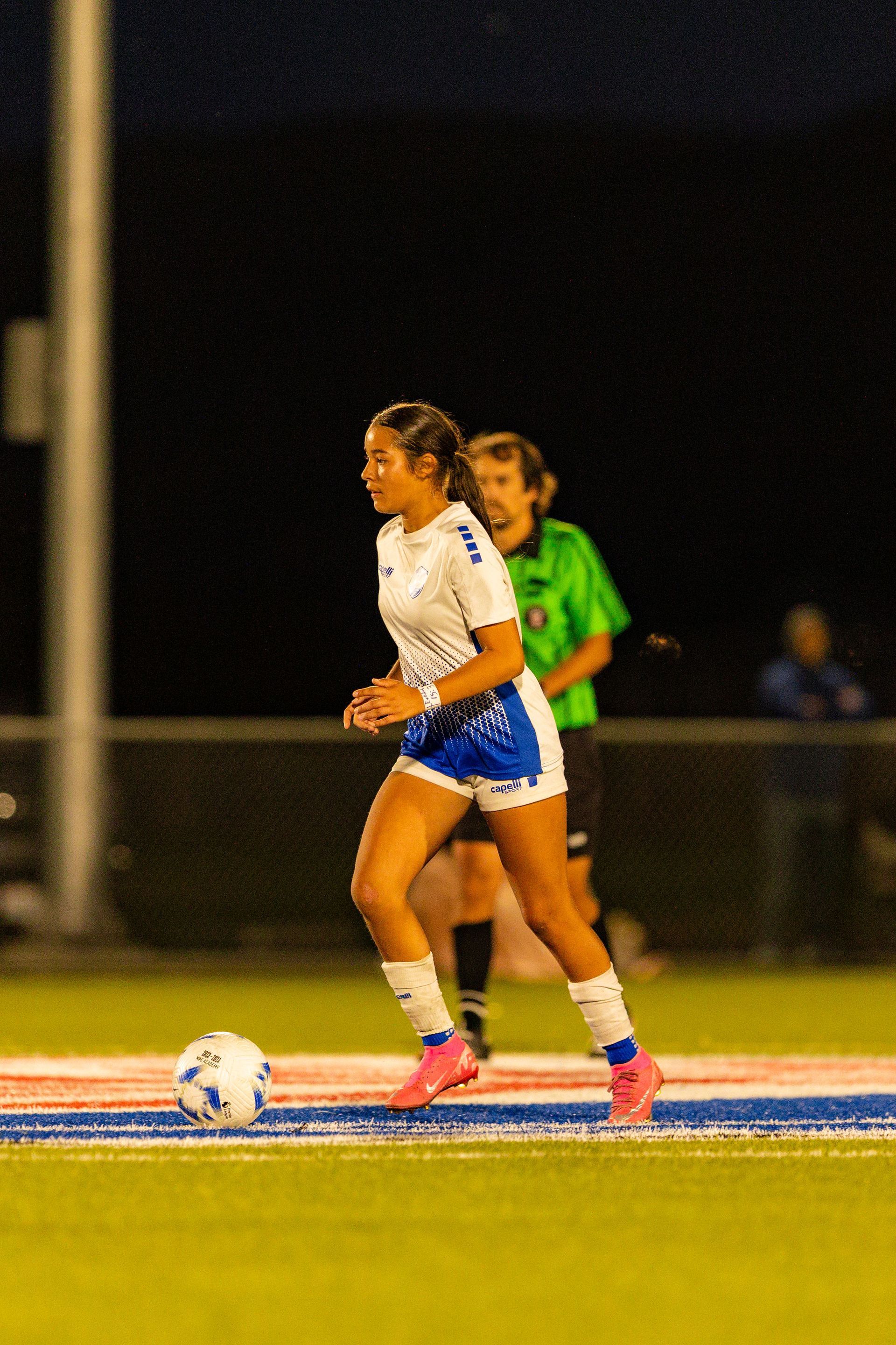A woman is playing soccer on a field at night.