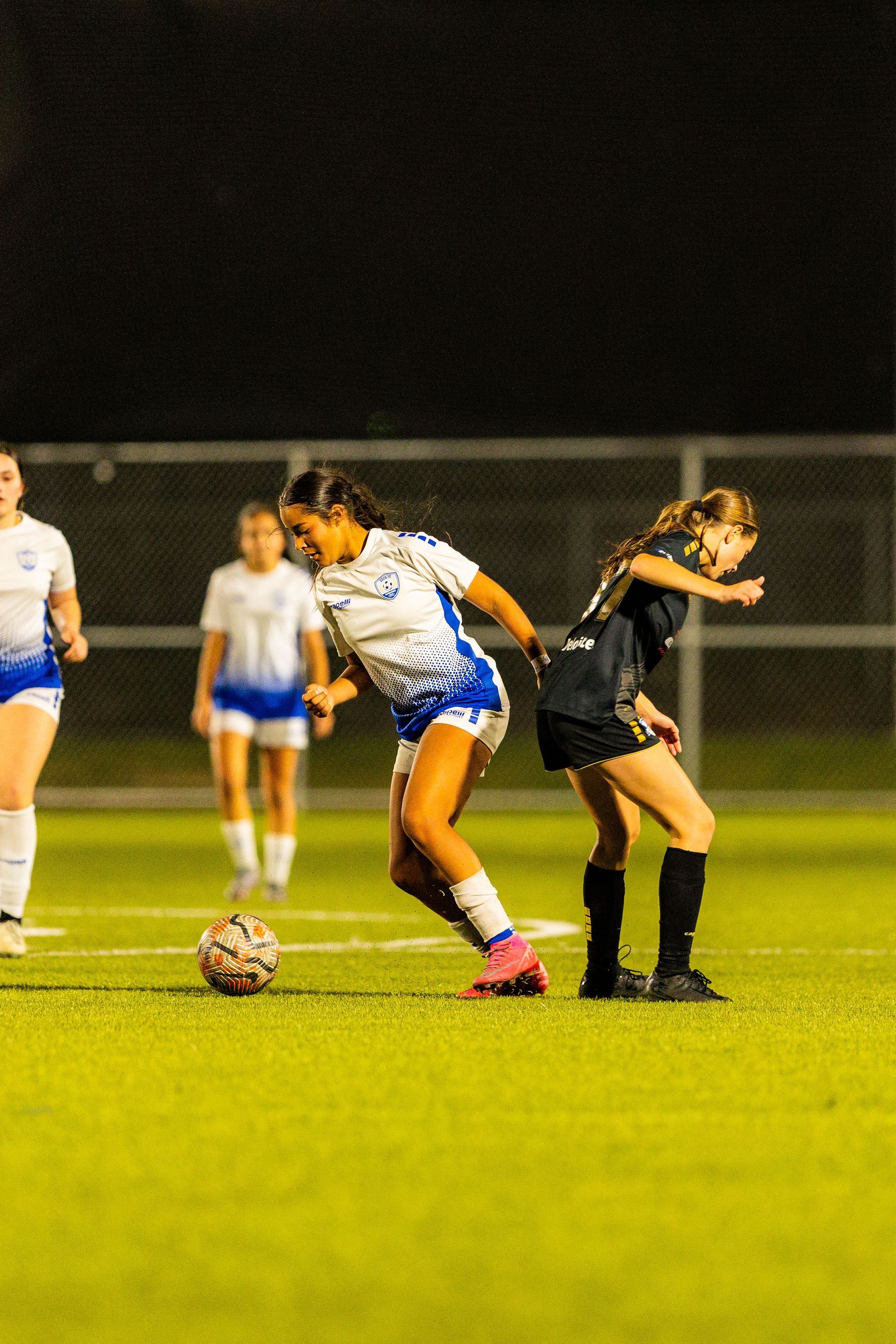 A group of girls are playing soccer on a field at night.