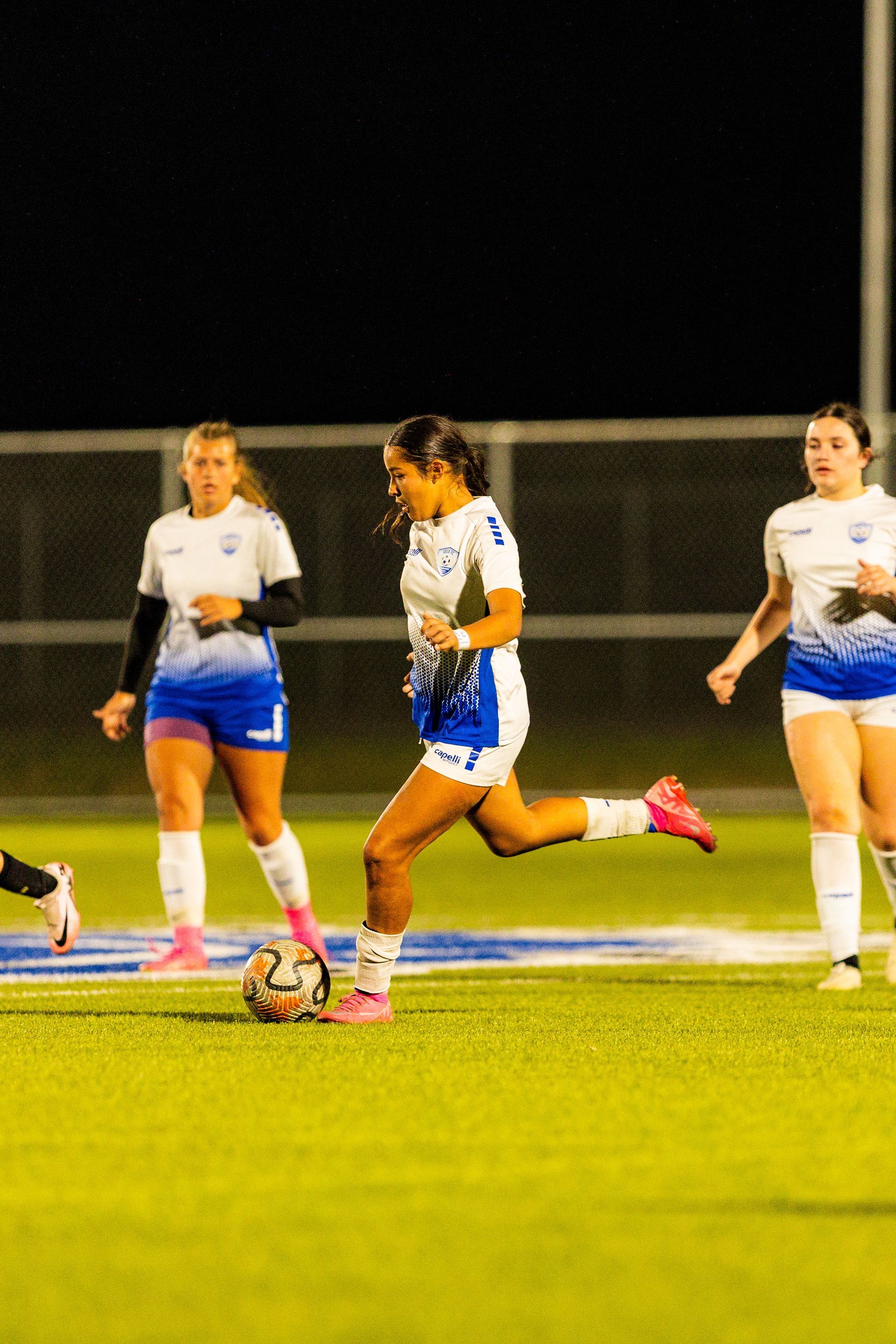 A group of women are playing soccer on a field at night.