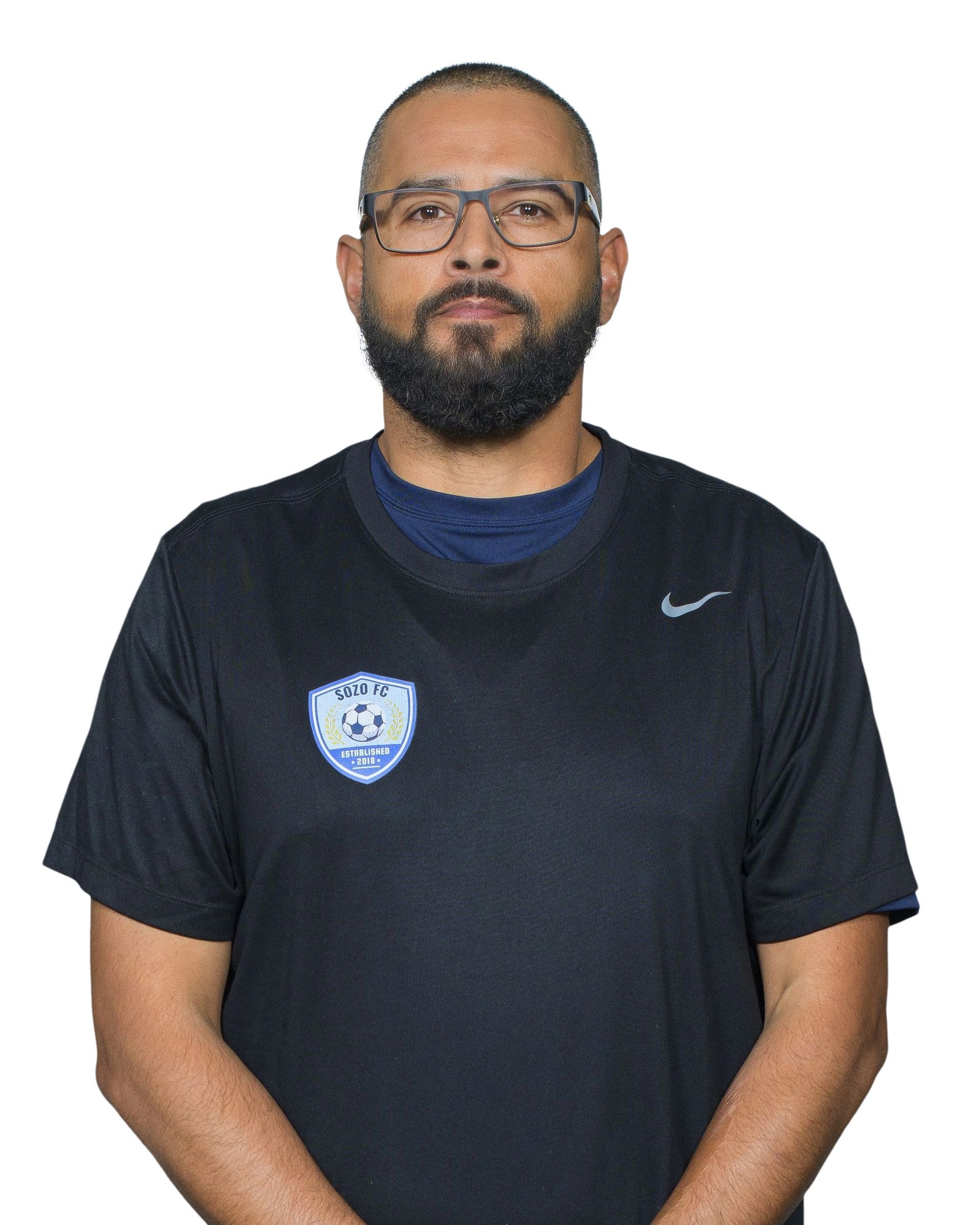 Man in glasses wearing a black Nike shirt with a blue crest, standing against a white background