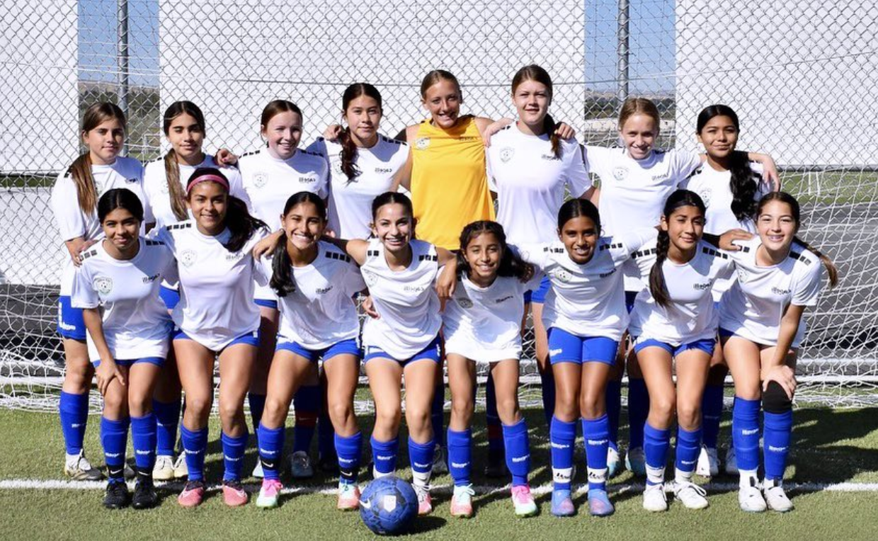 A group of young girls are posing for a picture on a soccer field.