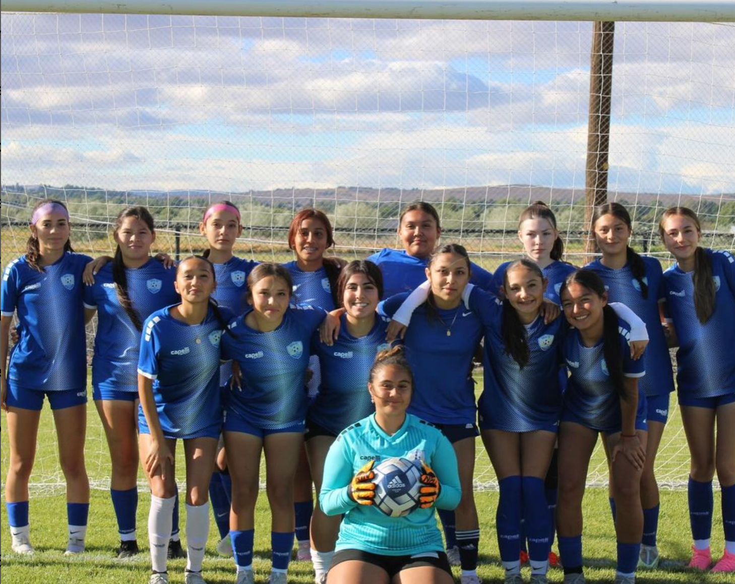 A group of young girls are posing for a picture on a soccer field.