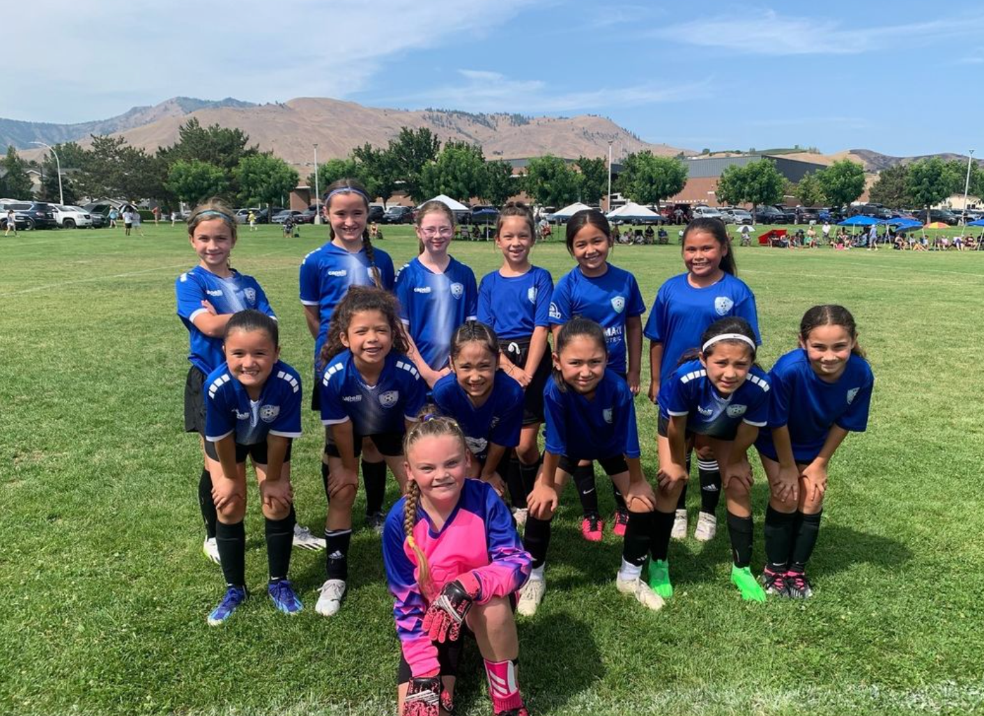A group of young girls are posing for a picture on a soccer field.
