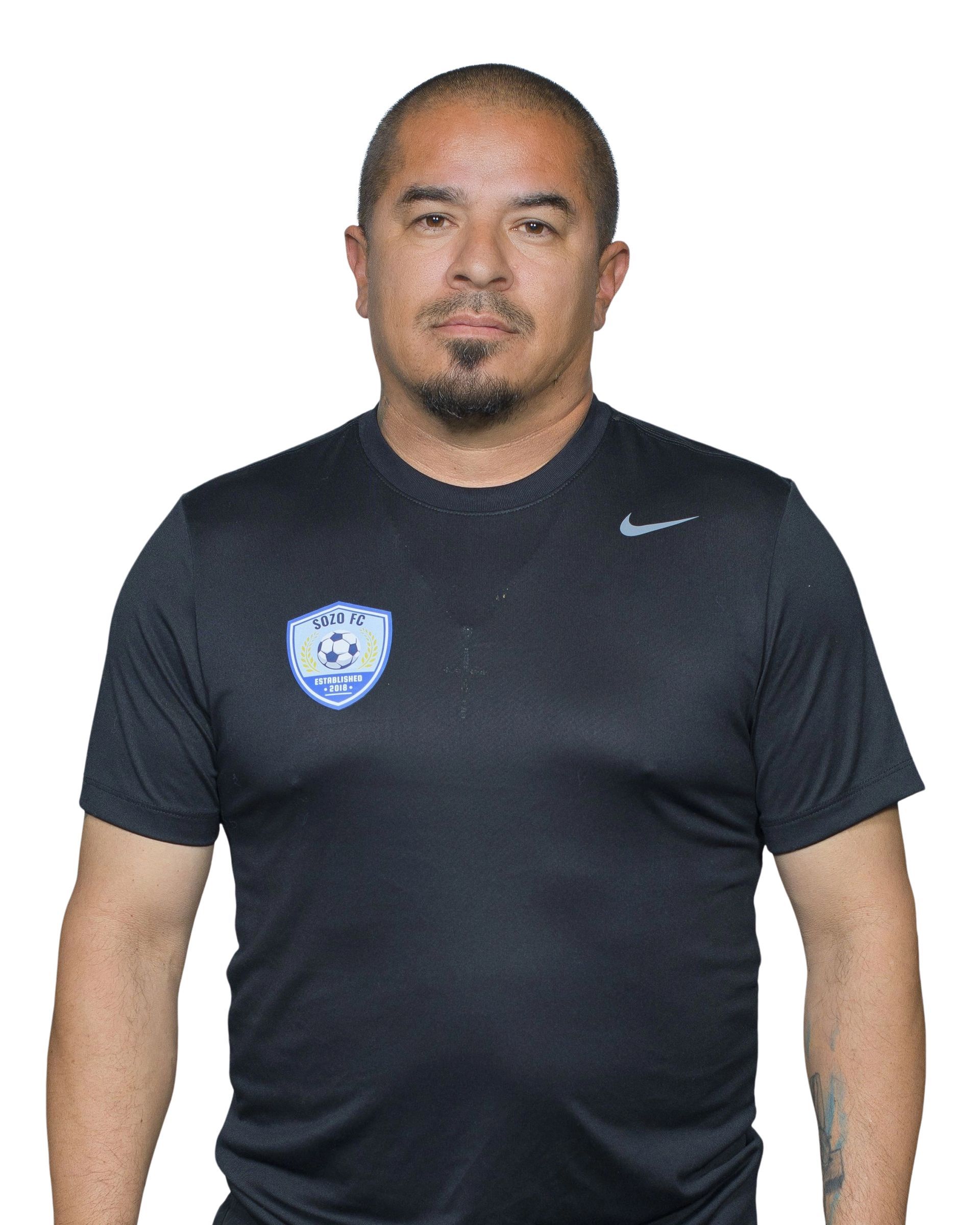 Man with shaved head and goatee smiling, wearing a pink button-down shirt.