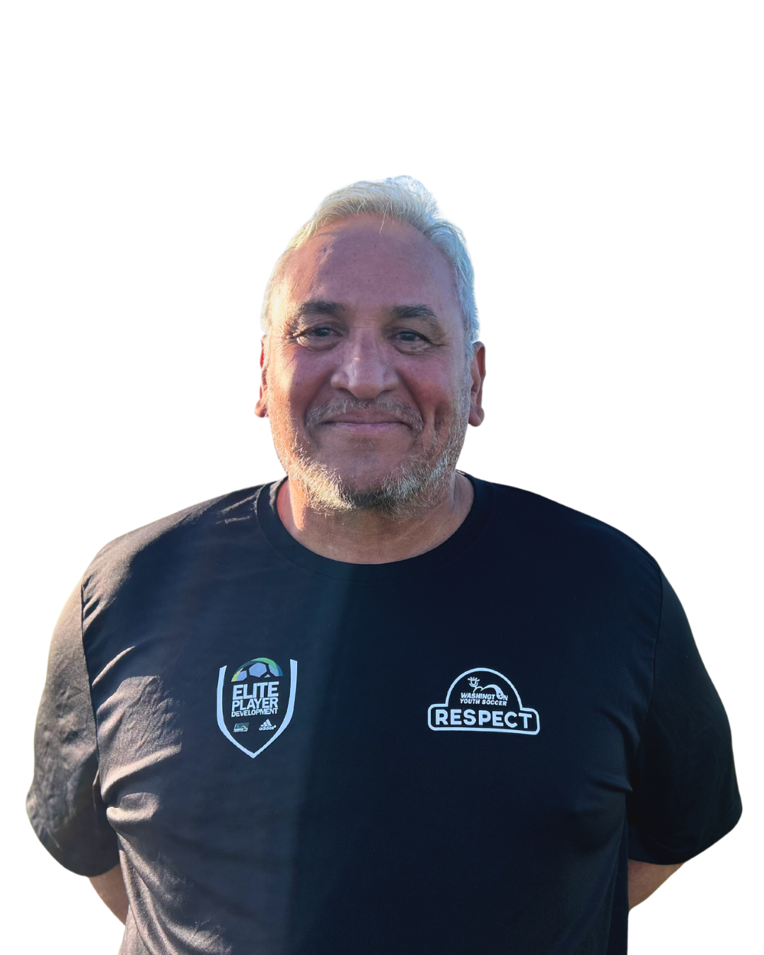 Man with graying hair wearing a black t-shirt, standing on a grassy field in front of a soccer goal and a blue sky.