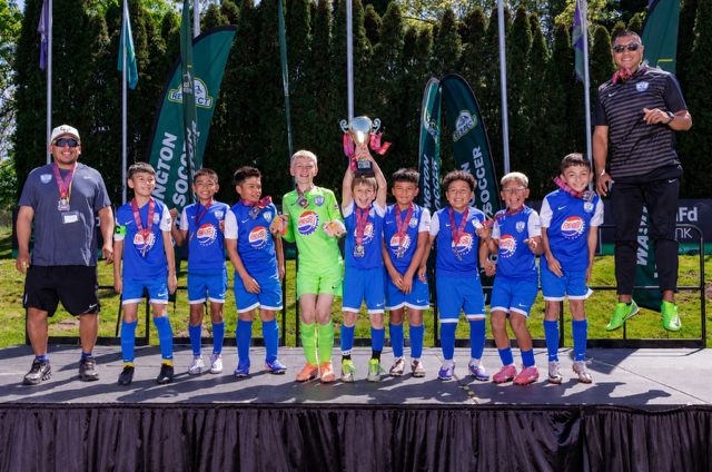 A group of soccer players are standing on a stage holding a trophy.