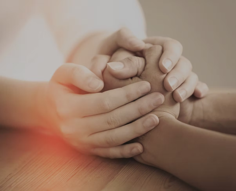 Two hands gently holding a child’s hand on a wooden table, with warm soft light