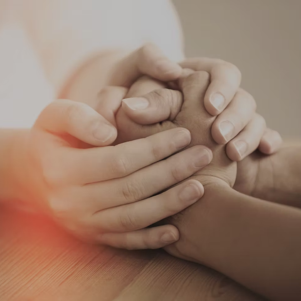 Two hands gently holding a child’s hand on a wooden table, with warm soft light