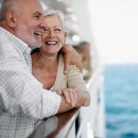 Smiling couple leaning on a boat railing, with blue water in the background