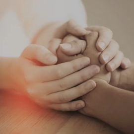 Two hands gently holding a child’s hand on a wooden table, with warm soft light