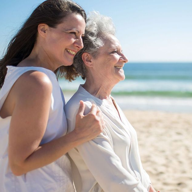 Older man seated while a smiling caregiver leans in to help him in a bright room