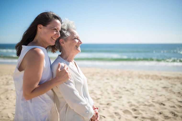 Older man seated while a smiling caregiver leans in to help him in a bright room