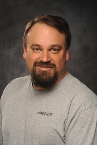 A person with a beard, wearing a grey T-shirt with the text 