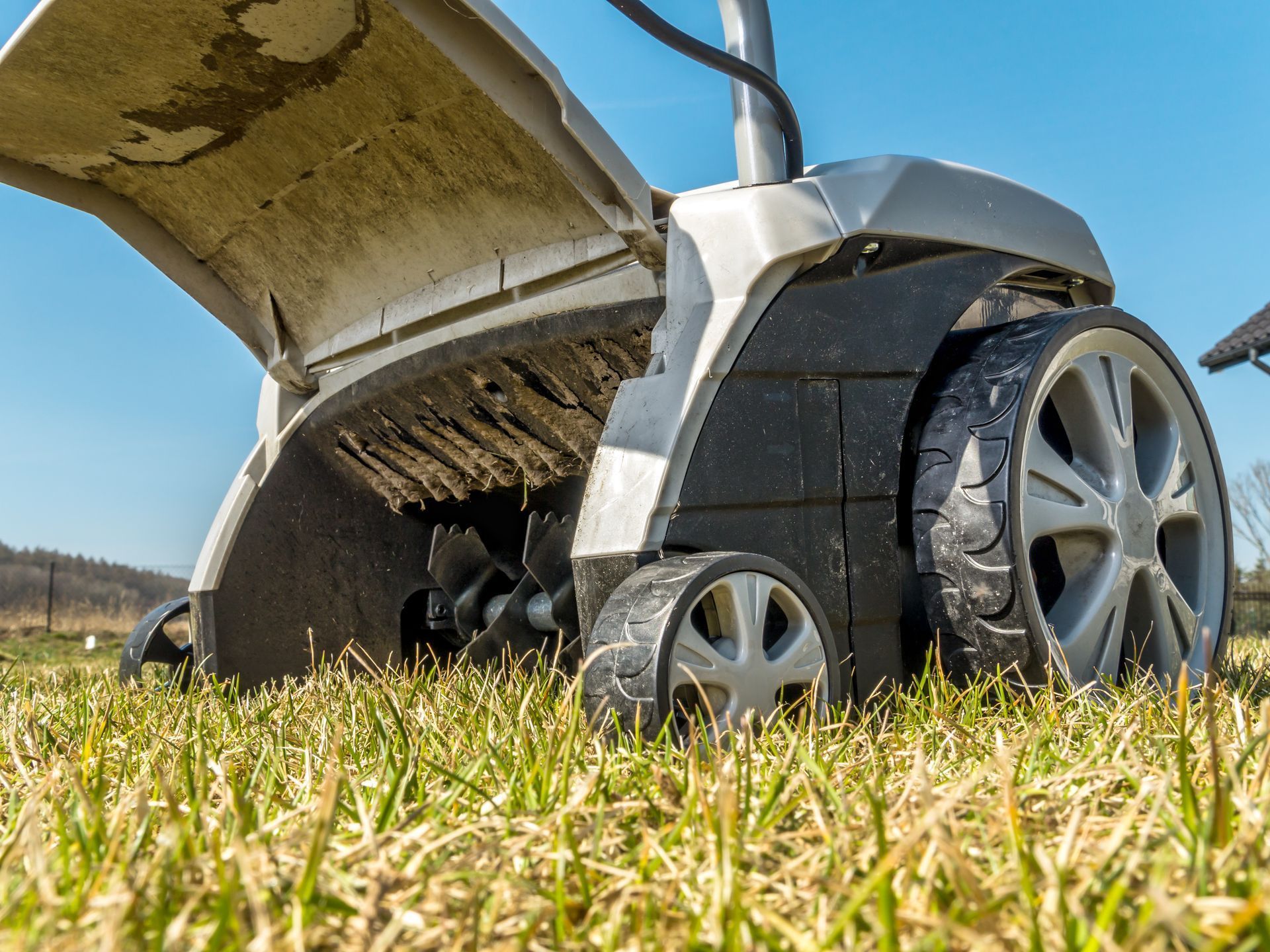 A low-angle view of a grey lawn scarifier sitting on a dry, grassy field against a clear blue sky.