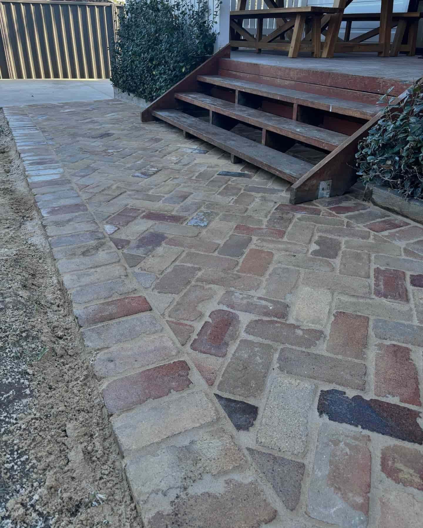 A brick walkway with wooden steps leading up to a house — Premier Bricks, Blocks & Pavers In Heatherbrae, NSW