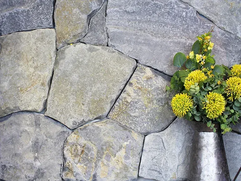 Stone wall with small silver vase holding yellow flowers — Premier Bricks, Blocks & Pavers In Heatherbrae, NSW