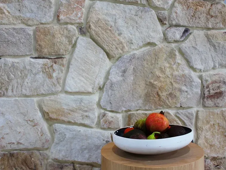 Bowl of fruit on a wooden table, in front of a natural stone wall — Premier Bricks, Blocks & Pavers In Heatherbrae, NSW