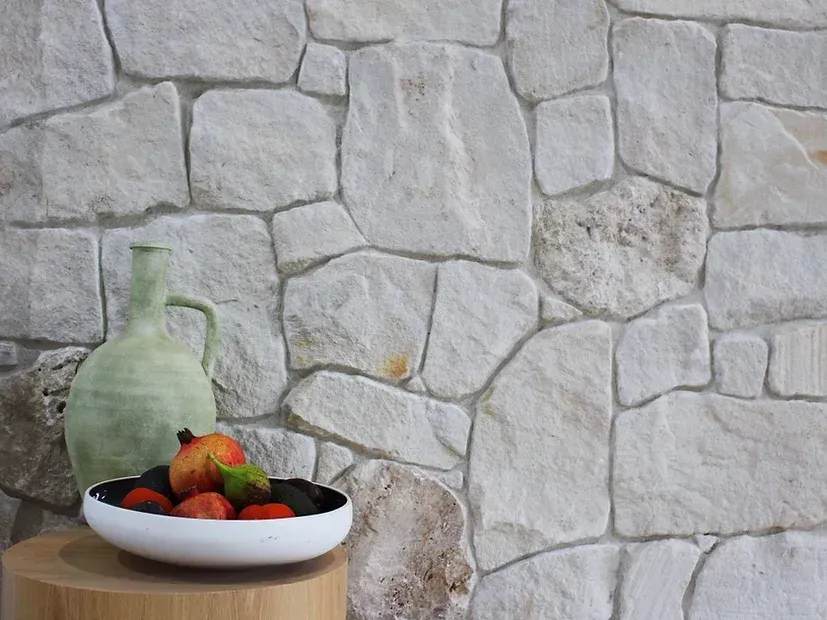 Stone wall with a green vase and bowl of fruit on a wooden table — Premier Bricks, Blocks & Pavers In Heatherbrae, NSW