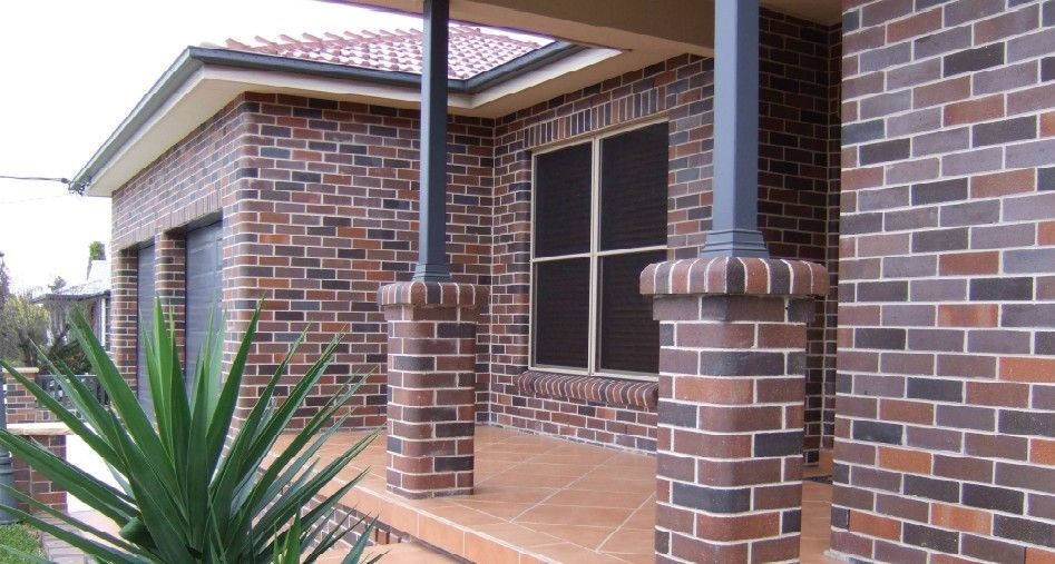 A white fence surrounds a brick wall in a backyard — Premier Bricks, Blocks & Pavers In Heatherbrae, NSW