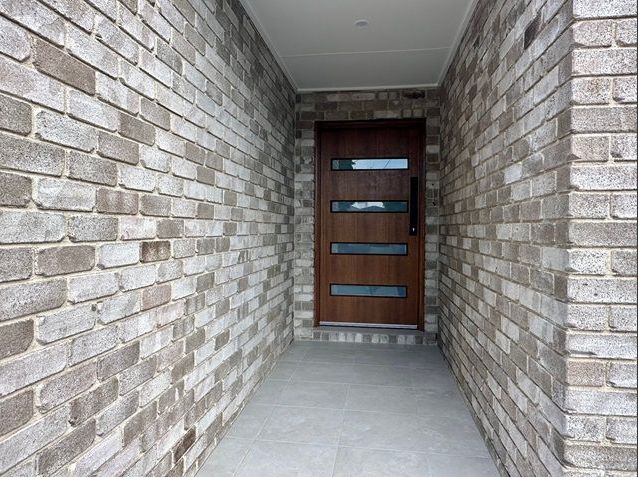 Brick entrance hallway with brown door and gray tile floor — Premier Bricks, Blocks & Pavers In Heatherbrae, NSW
