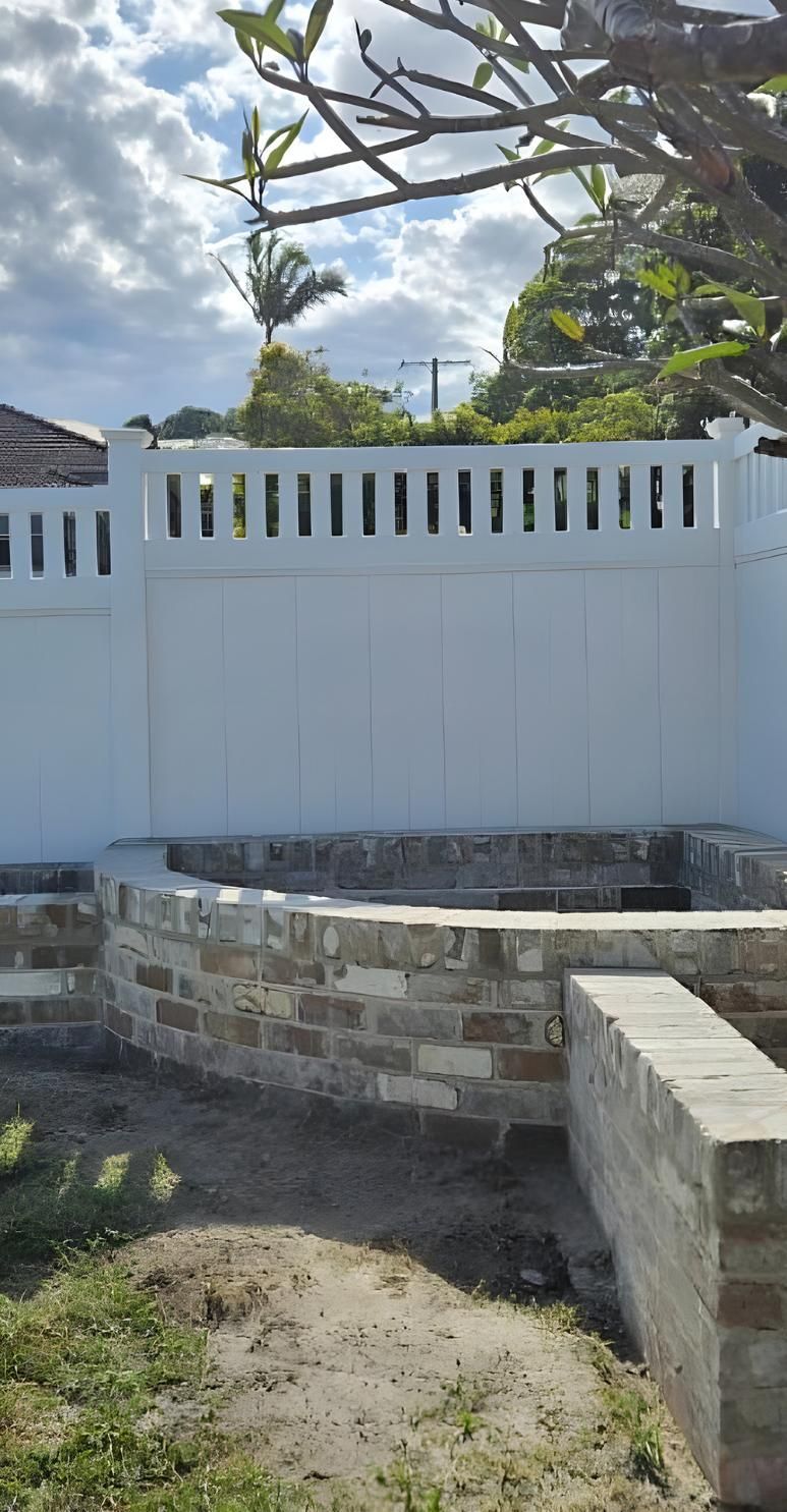 A White Fence Surrounds A Brick Wall In A Backyard — Premier Bricks, Blocks & Pavers In Newcastle, NSW