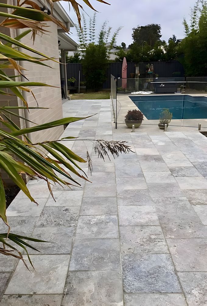 A Patio With A Swimming Pool In The Background And A Palm Tree — Premier Bricks, Blocks & Pavers In Cessnock, NSW