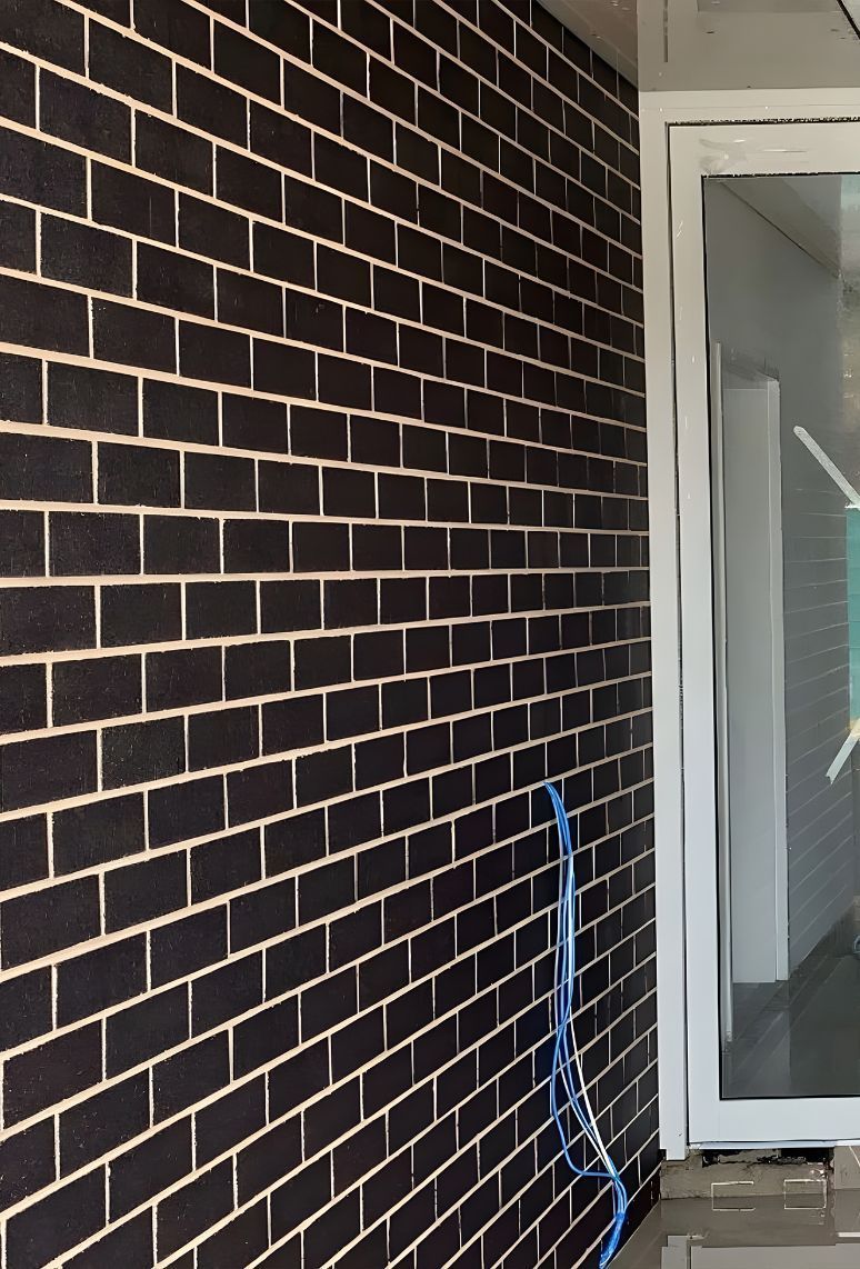 A Black Brick Wall With A White Door — Premier Bricks, Blocks & Pavers In Cessnock, NSW