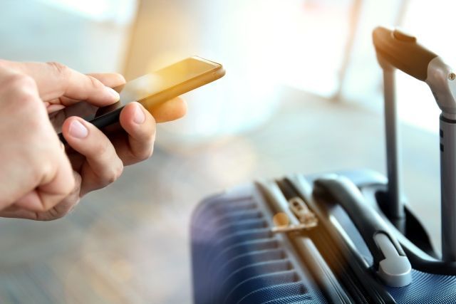A bértranszparencia tanácsadás útitárs csomagját jelképezi egy utazás közbeni pillanat (bőrönddel és mobillal)